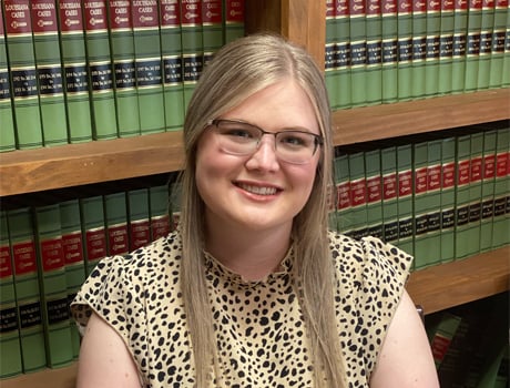 Smiling person with glasses in front of a bookshelf filled with law books.